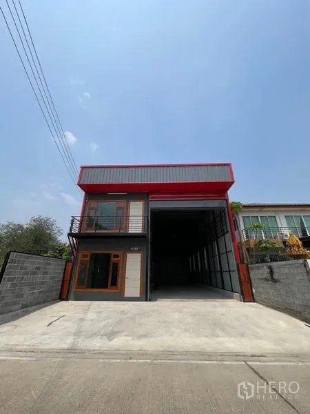 Warehouse for rent in Lam Luk Ka, Pathum Thani - Street-facing exterior of a modern high-bay warehouse with red trim, wide concrete driveway and gated side walls.
