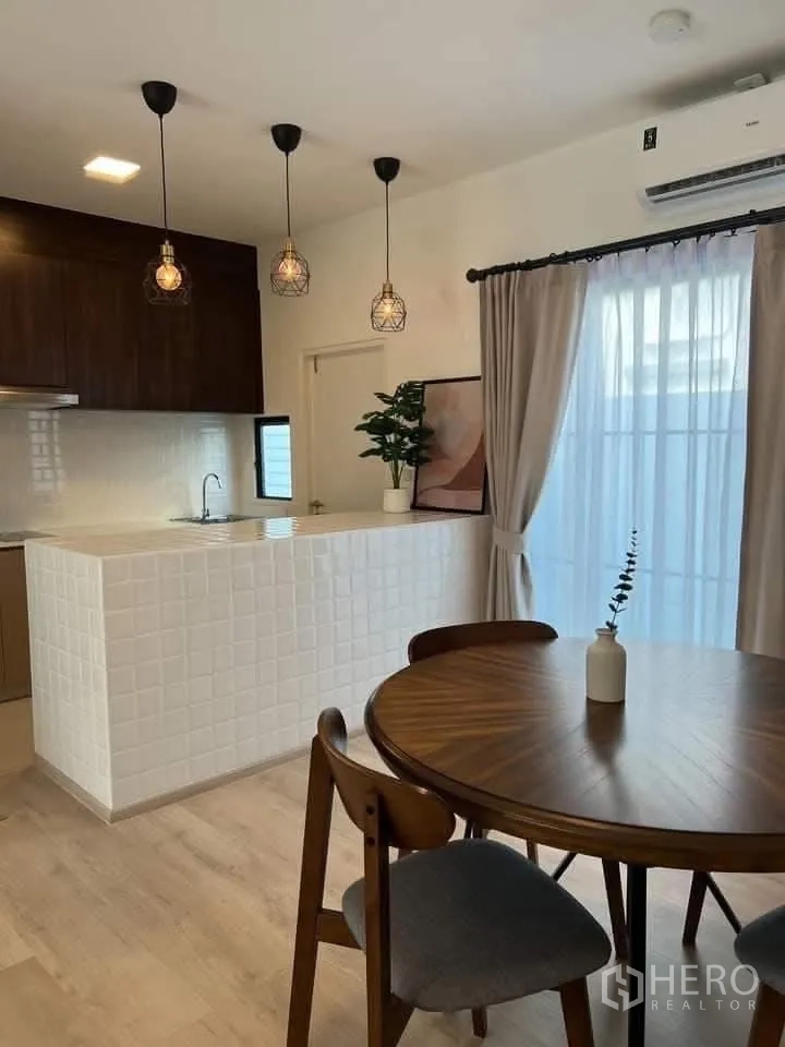 Townhouse for rent in Bang Phli, Samut Prakan - Dining area beside a white-tiled breakfast bar with pendant lights and curtains.