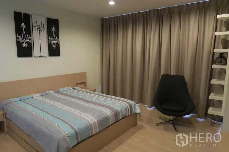 คอนโด ให้เช่าในHuai Khwang, Bangkok - ห้องนอนหลักเตียงคิง งานศิลป์ติดผนัง เก้าอี้หมุน และชั้นบิวท์อินกับผ้าม่านทึบ