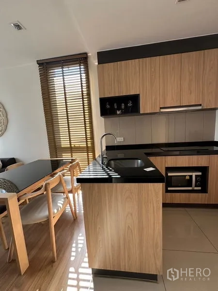 Condominium for rent in Watthana, Bangkok - L-shaped kitchen with hob, oven, and sink opening to the living area and balcony.