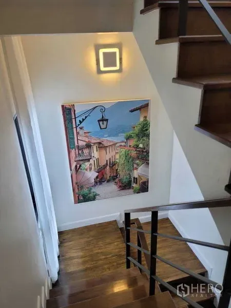 Detached House for rent or sale in Prawet, Bangkok - Wooden staircase with wall light and a large travel-themed painting.