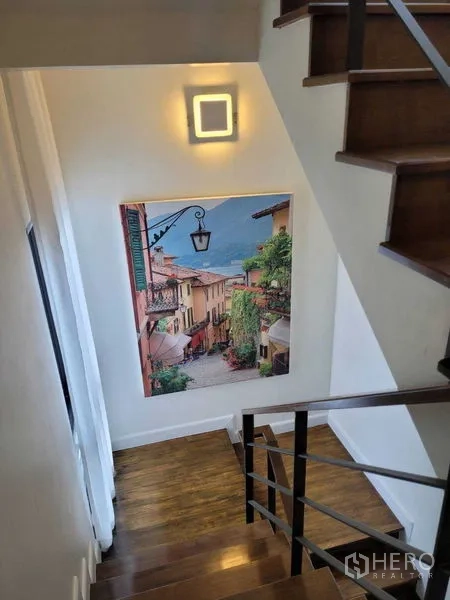 Detached House for rent or sale in Prawet, Bangkok - Wooden staircase with wall light and a large travel-themed painting.
