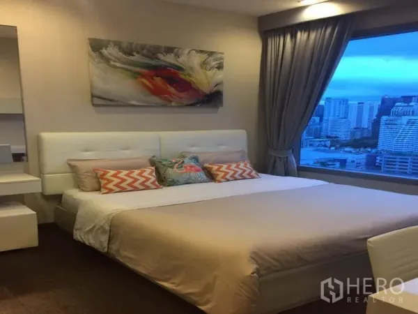 公寓 出租在Ratchathewi, Bangkok - 静谧卧室，软包床与装饰画，宽窗俯瞰城市黄昏景致。