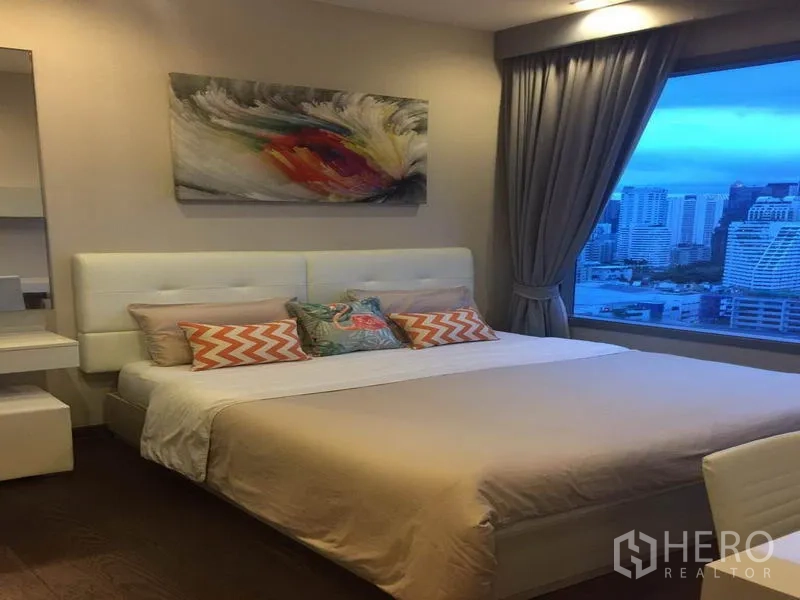 公寓 出租在Ratchathewi, Bangkok - 静谧卧室，软包床与装饰画，宽窗俯瞰城市黄昏景致。