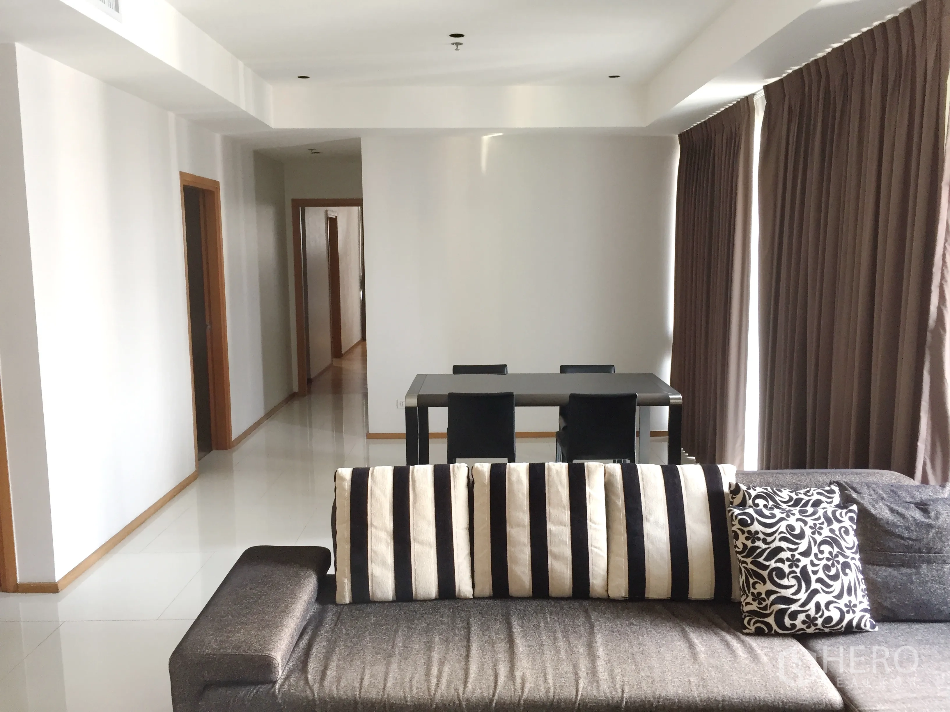 公寓 出租在Khlong Toei, Bangkok - 宽敞起居区，条纹靠垫沙发，四人餐桌，走廊通往卧室。