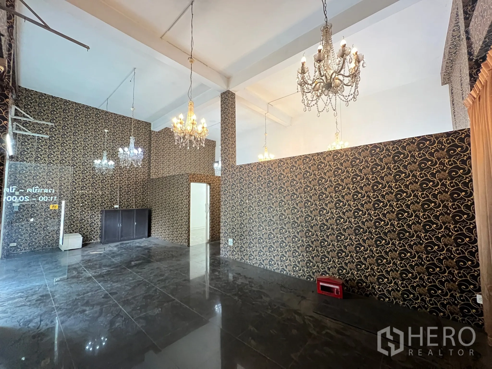 Shophouse for rent in Khlong Toei, Bangkok - Spacious retail hall with high ceiling, multiple chandeliers and patterned wallpaper.