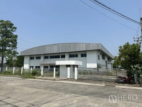 โรงงาน ให้เช่าในChon Buri - มุมมองด้านหน้าโรงงานสีขาวหลังคาเมทัลชีท โครงการรั้วรอบและประตูทางเข้าในนิคมอุตสาหกรรม