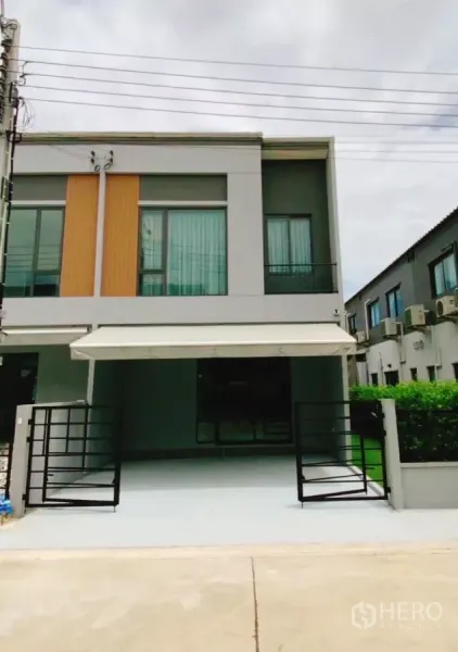 Townhouse for rent in Bang Phli, Samut Prakan - Modern two-storey townhouse facade with gated, covered two-car parking and a side garden.