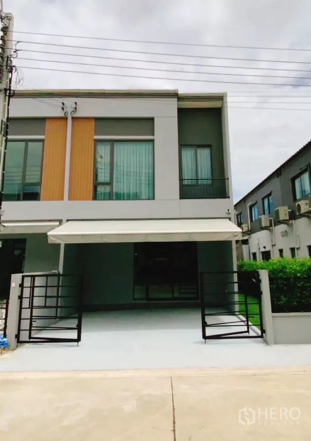 Townhouse for rent in Bang Phli, Samut Prakan - Modern two-storey townhouse facade with gated, covered two-car parking and a side garden.