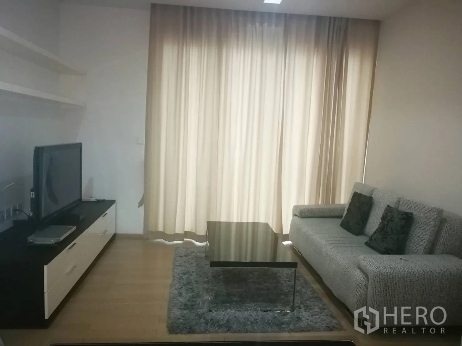 Condominium for rent in Khlong Toei, Bangkok - Modern living room with sofa, TV console, coffee table and floor-to-ceiling curtains.