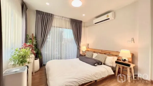 Detached House for rent or sale in Bang Khen, Bangkok - Bright bedroom with wooden bed, air conditioner, large windows and indoor plants.