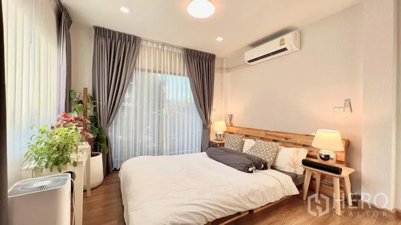 Detached House for rent or sale in Bang Khen, Bangkok - Bright bedroom with wooden bed, air conditioner, large windows and indoor plants.