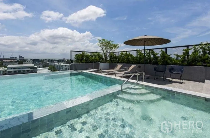 公寓 出租在Bang Na, Bangkok - 屋顶泳池设浅水阶梯与日光躺椅，俯瞰城市景观。