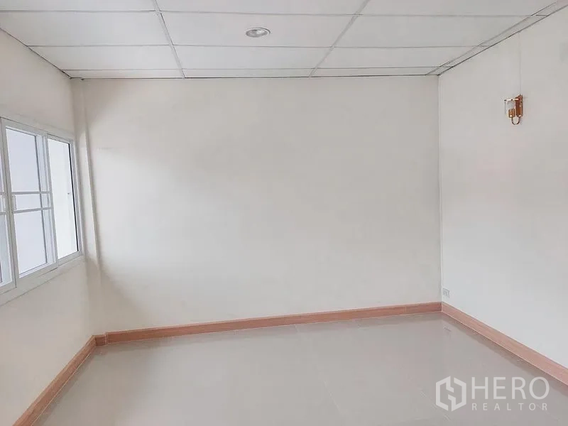 Townhouse for rent in Chatuchak, Bangkok - Empty corner room with window, drop ceiling, and glossy floor tiles.