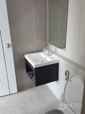 Townhouse for rent in Bueng Kum, Bangkok - Modern bathroom with wall-mounted vanity, large mirror, and neutral tiled walls.