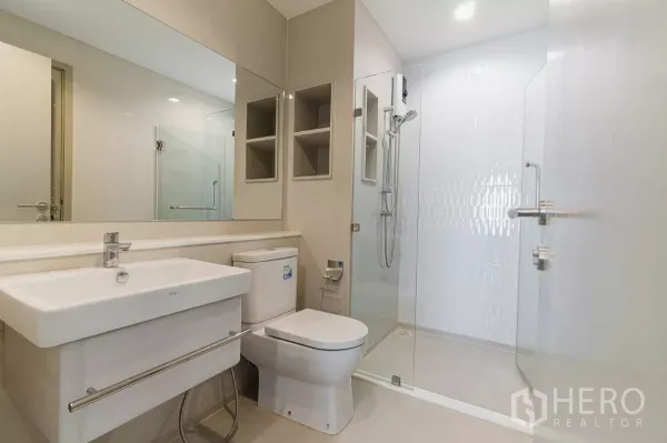 Condominium for rent in Chatuchak, Bangkok - Modern bathroom with large mirror, toilet and glass-enclosed shower.