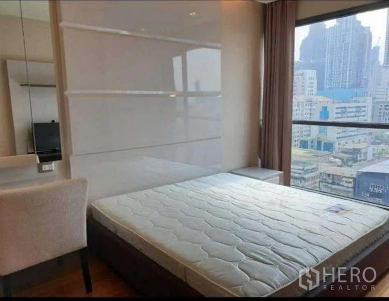 公寓 出租在Bang Rak, Bangkok - 阳光卧室配大床与梳妆台，窗外为曼谷城市全景。