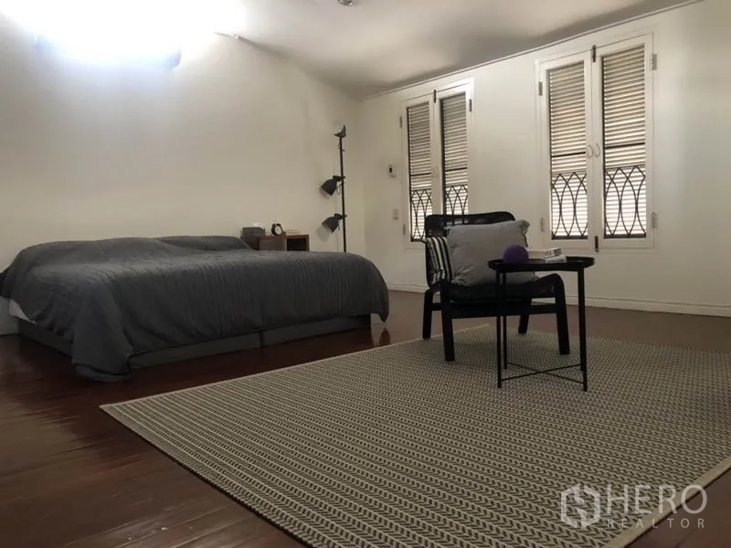 Detached House for rent in Bang Rak, Bangkok - Spacious bedroom with wood flooring, double windows with shutters, and neutral decor.