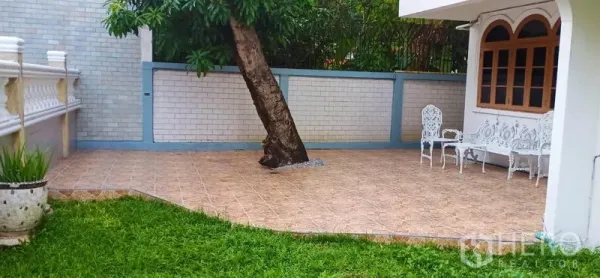 Detached House for rent in Watthana, Bangkok - Tiled patio with a tree and white outdoor seating next to the lawn.