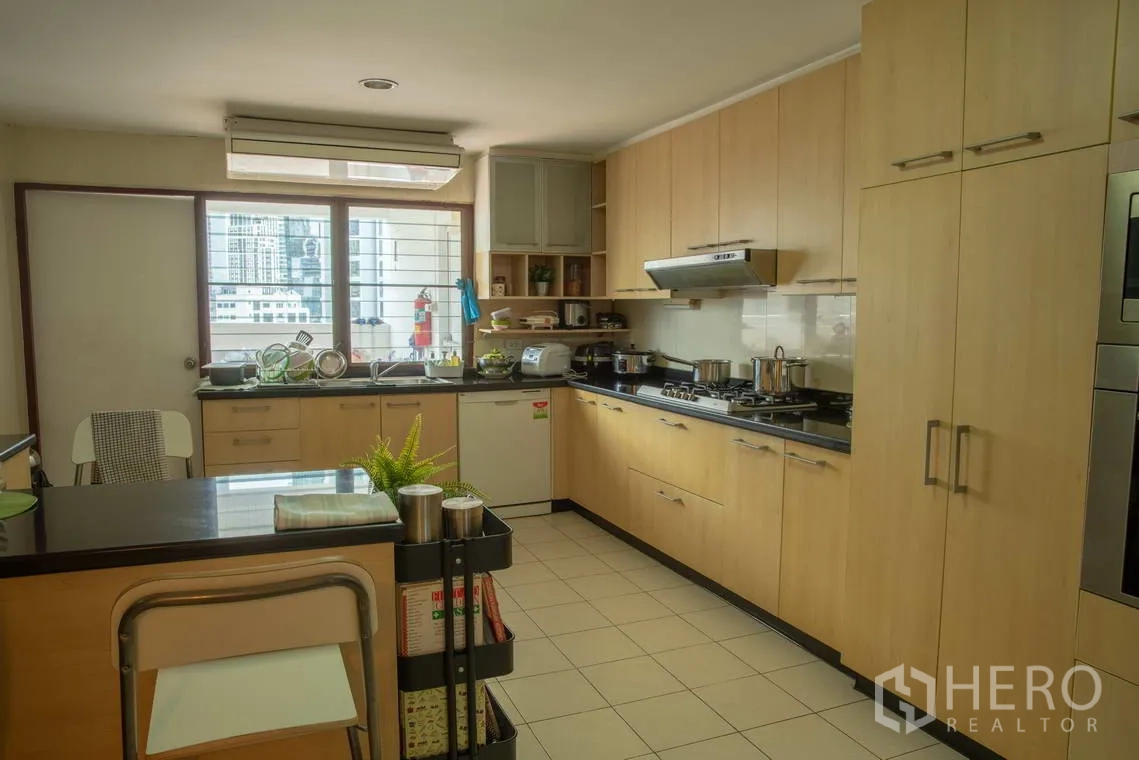อพาร์ทเมนท์ for rent in Khlong Toei, Bangkok - ครัวบิวท์อินโทนไม้พร้อมเตาแก๊ส ไอแลนด์ และหน้าต่างเห็นวิวเมือง.