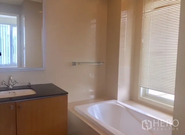 Condominium for rent in Watthana, Bangkok - Second bathroom with built-in vanity, bathtub and large mirror in soft lighting.