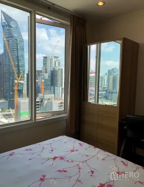 Condominium for rent or sale in Khlong Toei, Bangkok - Bedroom with large windows, wardrobe and desk, enjoying expansive skyline views.
