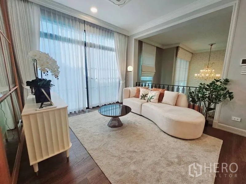 Detached House for rent or sale in Saphan Sung, Bangkok - Cozy upstairs family lounge with curved sofa, floor‑to‑ceiling drapes and balcony doors.