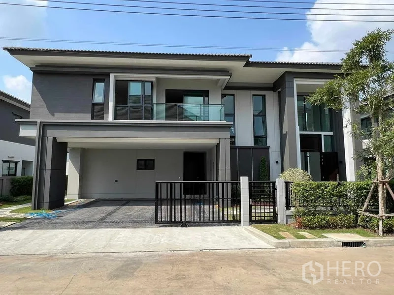 独立式住宅 出租在Khlong Sam Wa, Bangkok - 房屋正立面，两层结构，带阳台、宽敞车库与前院大门。