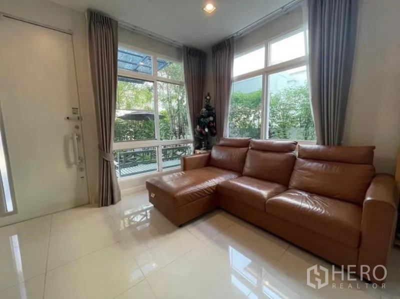 Detached House for rent in Lat Krabang, Bangkok - Corner lounge with L-shaped leather sofa, tall windows and garden view