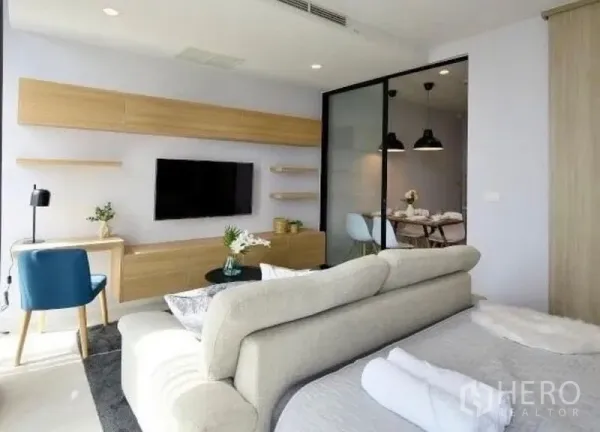 Condominium for rent in Pathum Wan, Bangkok - Living zone with wall-mounted TV, light wood cabinetry, and a sliding glass partition to the dining room.