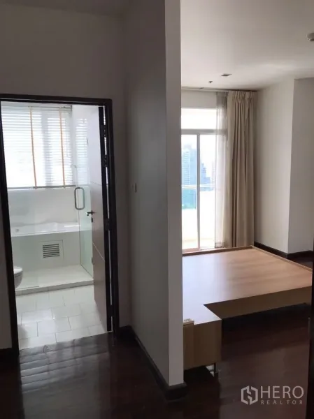 公寓 出租在Watthana, Bangkok - 公寓过道通向采光良好的卧室平台区与带玻璃门的浴室，窗外引入城市光线。