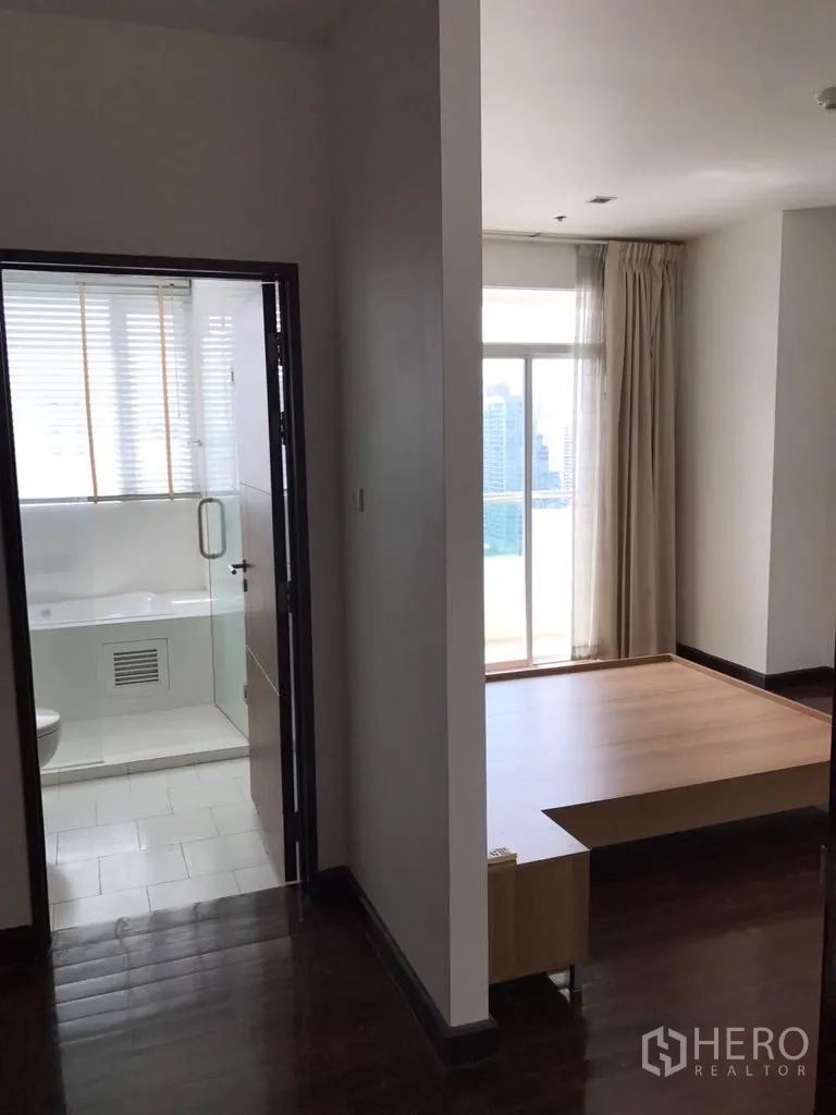 公寓 出租在Watthana, Bangkok - 公寓过道通向采光良好的卧室平台区与带玻璃门的浴室，窗外引入城市光线。
