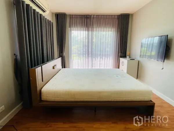 Detached House for sale in Lam Luk Ka, Pathum Thani - Air-conditioned bedroom with balcony access, grey curtains and wall-mounted TV.