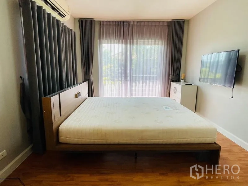Detached House for sale in Lam Luk Ka, Pathum Thani - Air-conditioned bedroom with balcony access, grey curtains and wall-mounted TV.