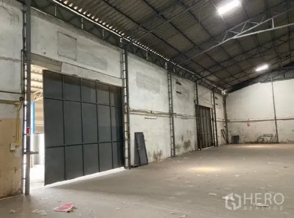 Factory for rent in Samut Prakan - Industrial hall showing large sliding steel doors, bright ceiling lights and a wide clear-span floor.