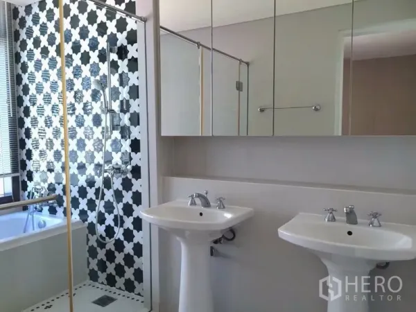 Condominium for rent in Khlong Toei, Bangkok - Modern bathroom with double pedestal sinks, mirrored cabinets, patterned shower wall and bathtub.