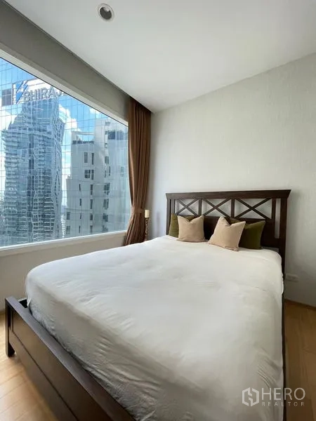 Condominium for rent in Watthana, Bangkok - Bedroom with wooden bedframe and skyline view through a picture window.