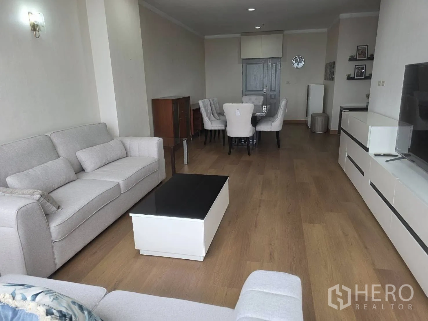 Condominium for rent in Khlong Toei, Bangkok - Long lounge with sofas, TV console and wood floors.
