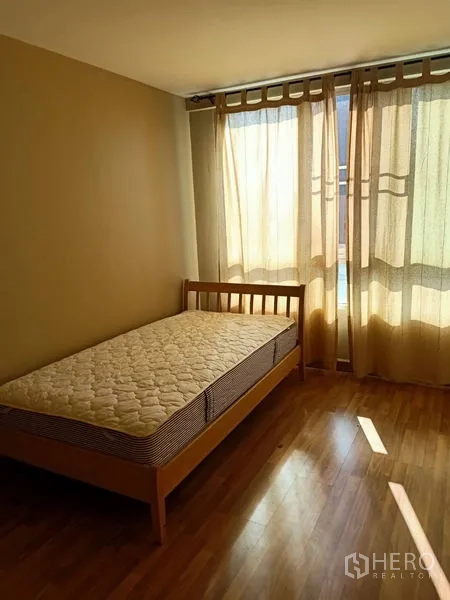 Condominium for rent in Khlong Toei, Bangkok - Sunny bedroom with a single bed and sheer curtains over floor-to-ceiling windows.
