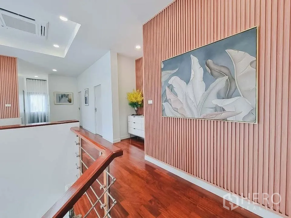 独栋房屋 for rent or sale in Bang Phli, Samut Prakan - 楼上走廊，木质竖向饰面墙、装饰画与楼梯扶手。