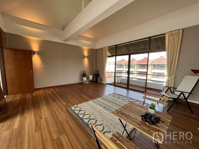 Townhouse for rent or sale in Suan Luang, Bangkok - High-ceiling family room with exposed beams and sliding glass doors to the balcony.