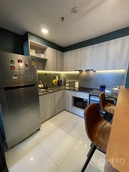 Condominium for sale - Modern U-shaped kitchen with wood cabinets, LED backsplash, bar counter and stainless refrigerator.