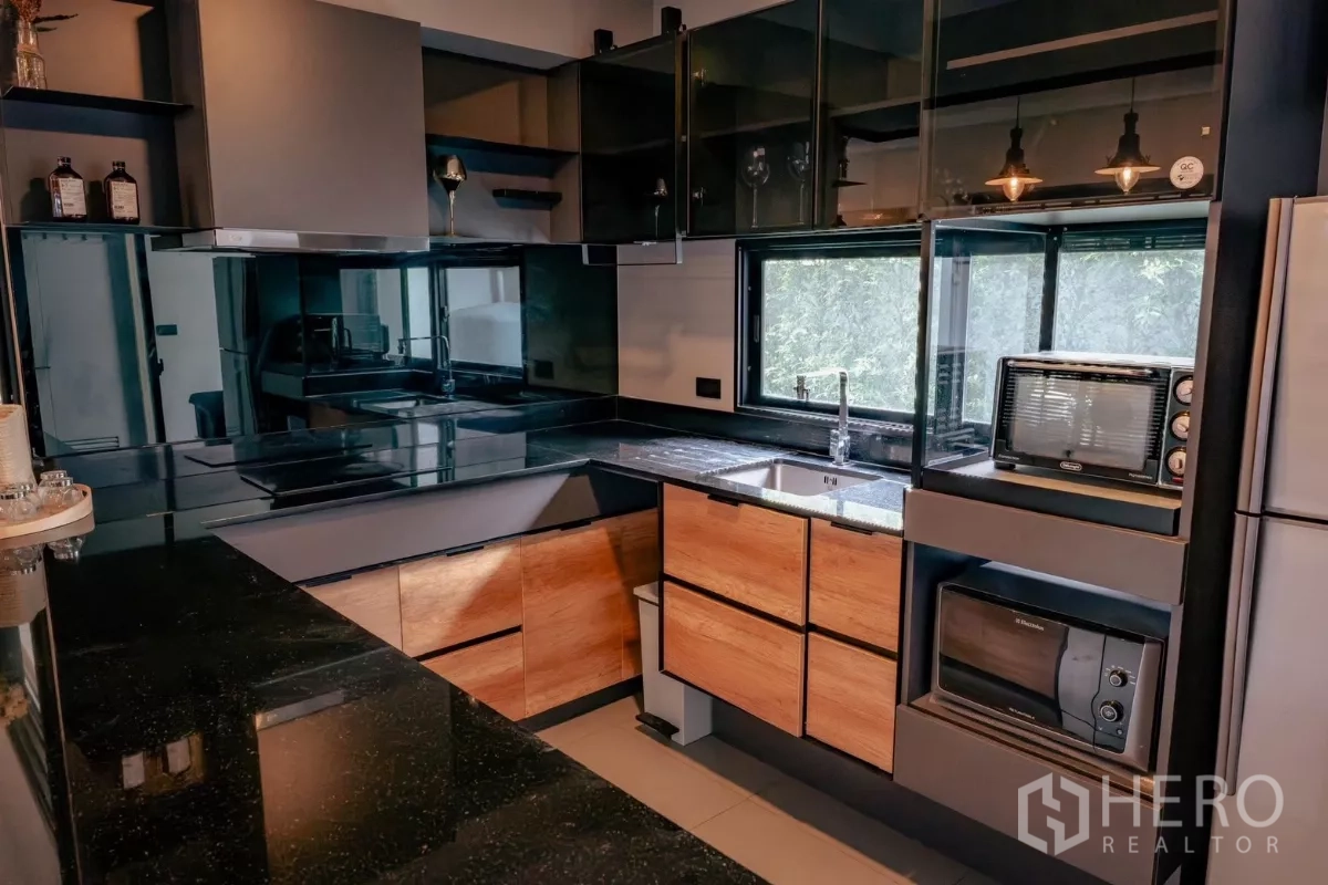 Detached House for rent or sale in Bang Phli, Samut Prakan - Contemporary L‑shaped kitchen with black stone counters, wood cabinetry and glass uppers.