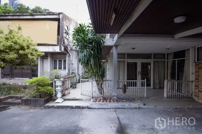 独立式住宅 出租在Khlong Toei, Bangkok - 房屋前院带有遮雨车位、成熟绿植和玻璃入户门，靠近BTS Thonglor。
