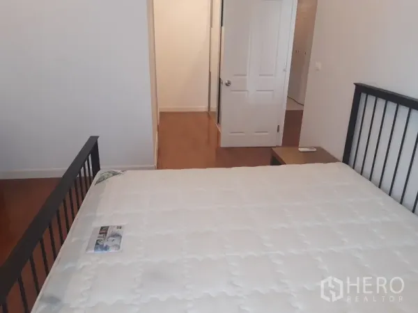 Condominium for rent in Khlong Toei, Bangkok - Master bedroom facing the doorway with wood floors, bedside table and simple décor.