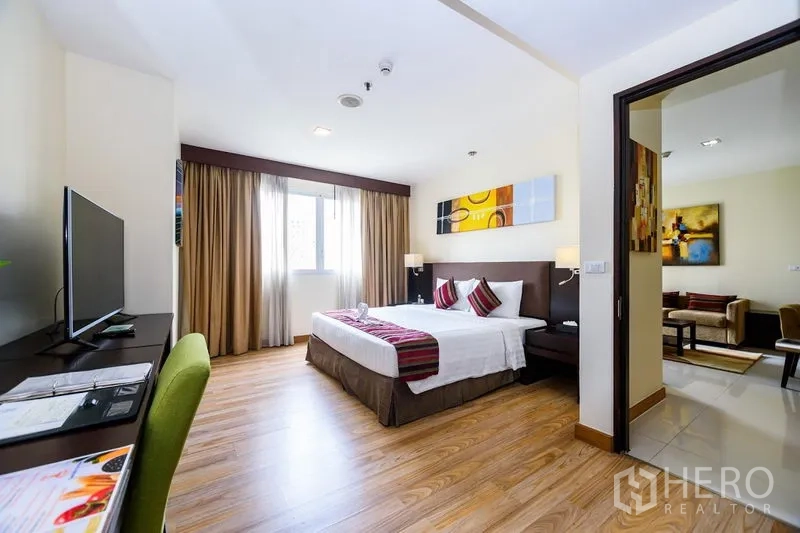 Condominium for rent in Khlong Toei, Bangkok - Spacious master bedroom with king bed, work desk with TV, wood floors and a large window.