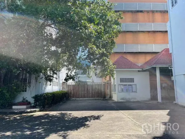 Factory for rent in Phra Samut Chedi, Samut Prakan - Shaded courtyard with mature tree and access gate between site buildings.