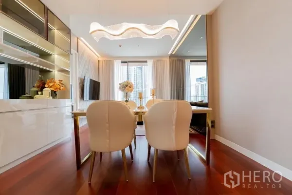 Condominium for rent in Watthana, Bangkok - Bright dining area with wave chandelier, gold table, white chairs and floor‑to‑ceiling windows overlooking the city.