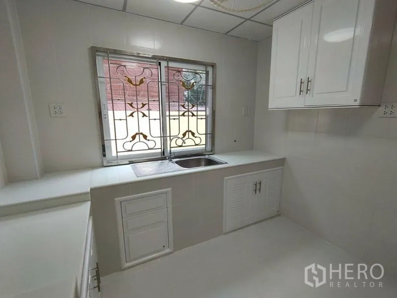 Detached House for rent in Khlong Toei, Bangkok - White built-in kitchen with stainless sink, upper cabinets and decorative window grills.