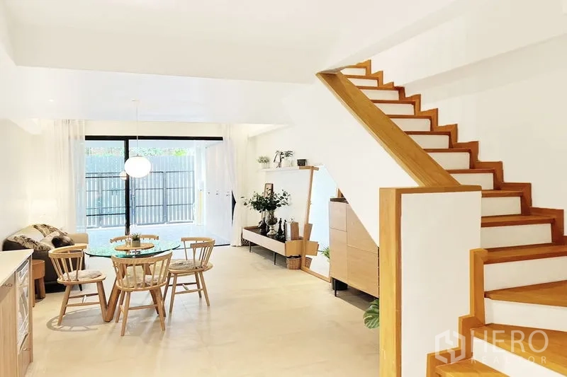 Townhouse for rent in Khlong Toei, Bangkok - Ground-floor living–dining space with wooden staircase and wide sliding doors to the front.